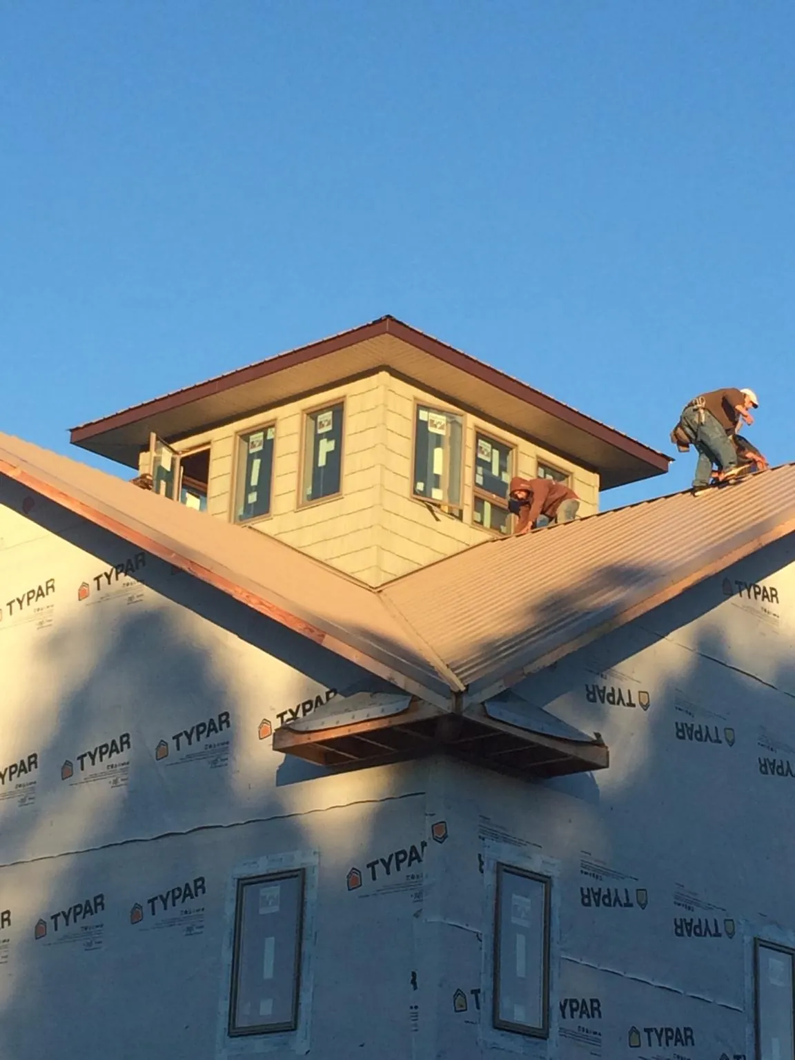 Roofers working around a rooftop cupola on a new metal roof at sunset — Roof Waterproofing in Rochester by Roofing Brothers